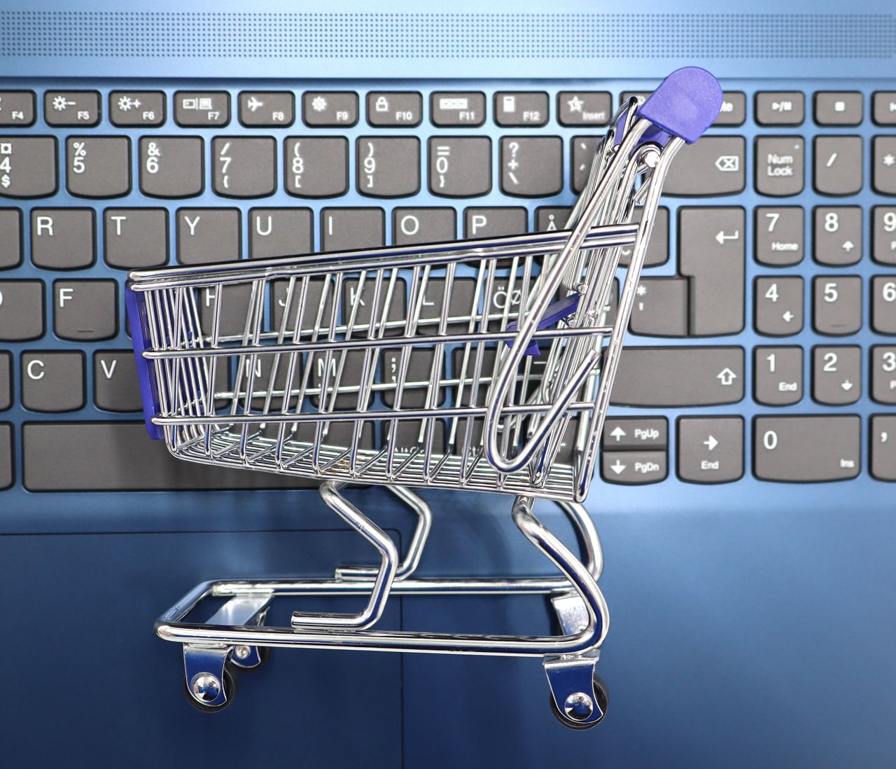 mobile-02 A miniature shopping cart placed on a laptop keyboard symbolizing online shopping and e-commerce.